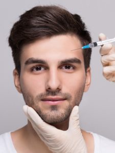 young man receiving sculptra injection in cheek from professional in latex gloves