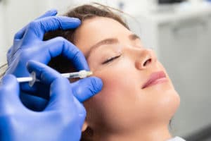 young woman receiving sculptra injection in cheek from professional in blue gloves