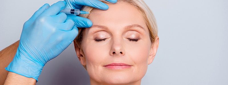 middle aged woman receiving sculptra injection in forehead from professional in blue gloves