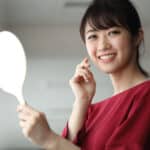 Young woman holding mirror and smiling at her clear skin after IPL photo rejuvenation