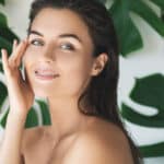 Woman in front of palm fronds touches her healthy, smooth skin