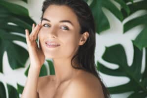 Woman in front of palm fronds touches her healthy, smooth skin
